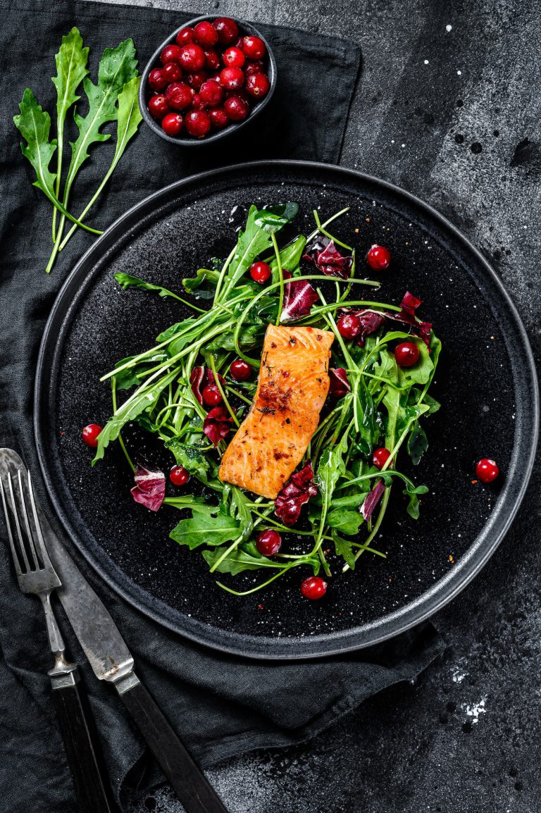 Seafood salad with trout, arugula, lettuce and cranberries. Black background. Top view